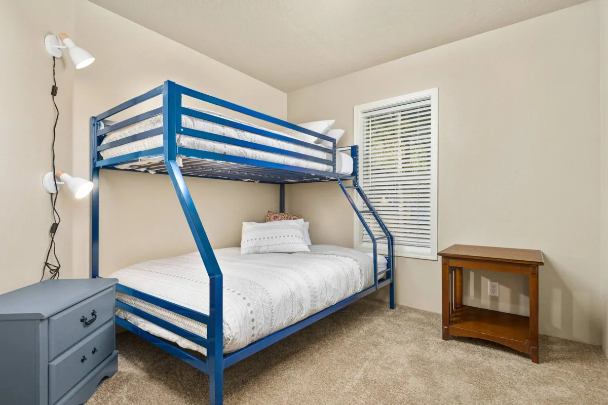 A cheerful third bedroom with a twin-over-full bunk bed, a nightstand, and a bright window. The space feels playful and cozy, perfect for children or friends, with a sense of nesting and fun sleepovers.