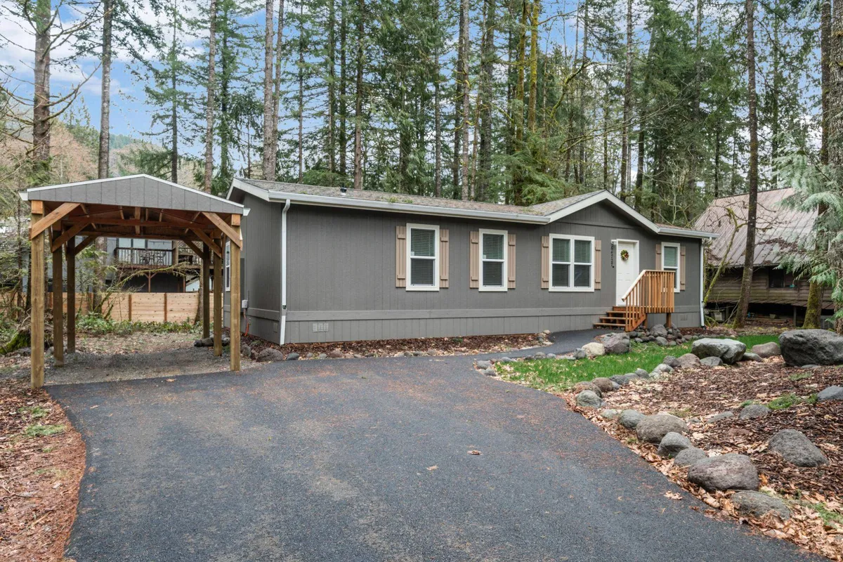 An exterior shot of the modular home featuring a wooden carport, landscaped stone accents, and forested surroundings. The view hints at the possibilities for outdoor relaxation and activities such as nature walks and stargazing.