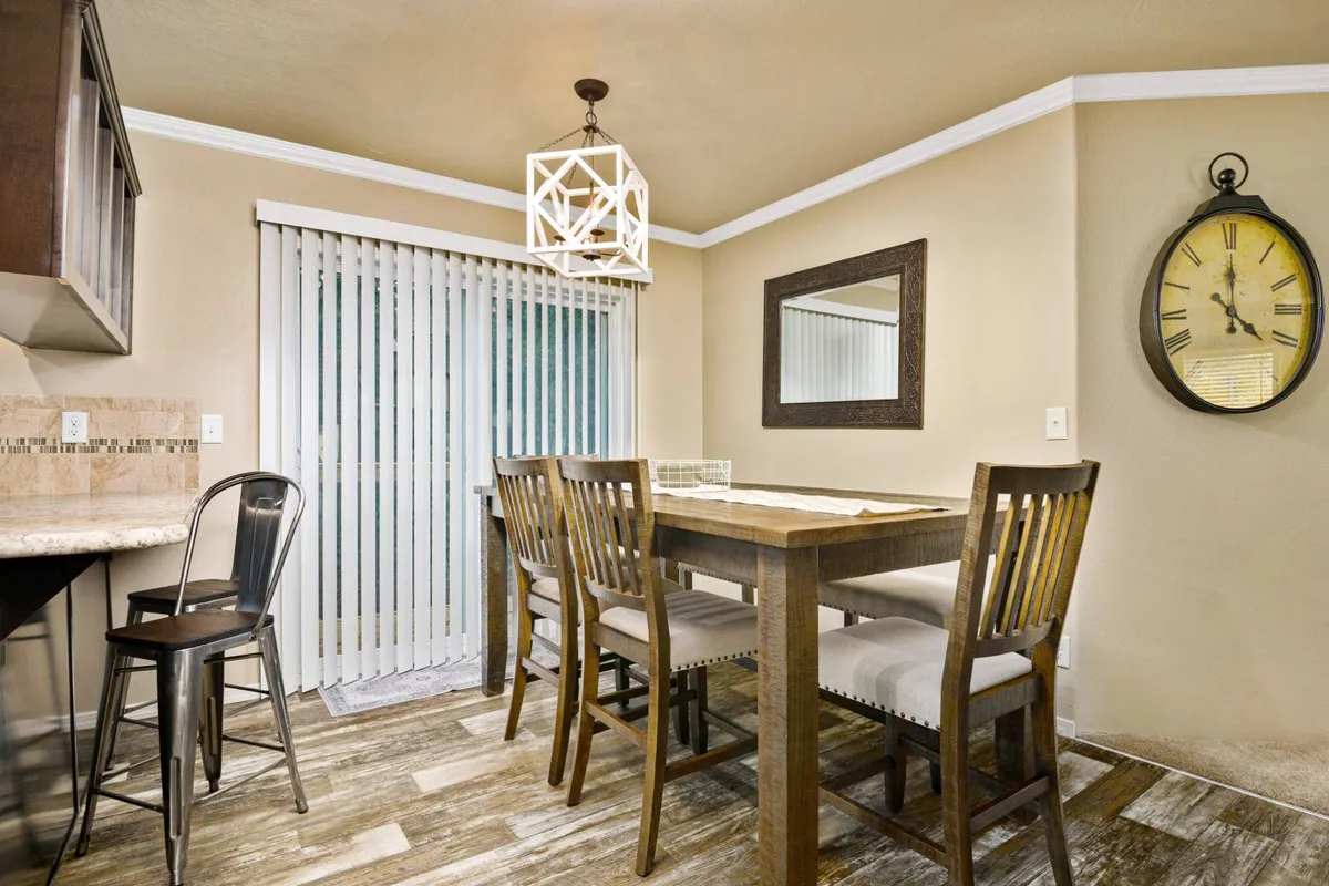 A warm and welcoming dining area is depicted, featuring a wooden dining table under a chandelier, with a decorative mirror and clock on the wall. The setup encourages shared meals and meaningful conversations, exuding a sense of intimacy and celebration.