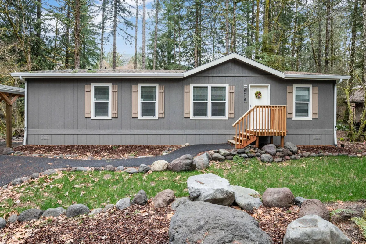 This image captures the front porch of the home surrounded by a landscaped yard, with natural rock formations and greenery creating a welcoming outdoor setting. The view suggests a seamless connection between the home and its natural surroundings.