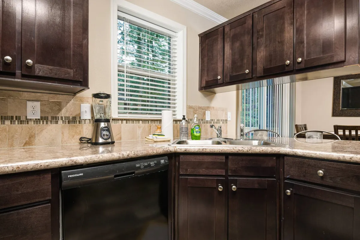 A functional, well-lit kitchen featuring a granite countertop and dark wood cabinetry, with a window allowing natural light to filter in. Appliances and a comfortable layout suggest a space that is equally suited for preparing snacks or morning coffee before heading out to explore local markets.