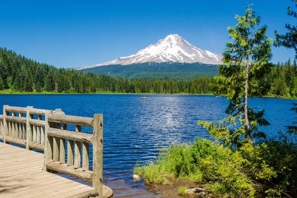 A tranquil lakeside scene featuring a wooden dock stretching over the water, surrounded by trees and framed by mountain views. The area radiates calm and possibility for boating, fishing, or simply relaxing, echoing the communal, vacation community vibe described in the section.