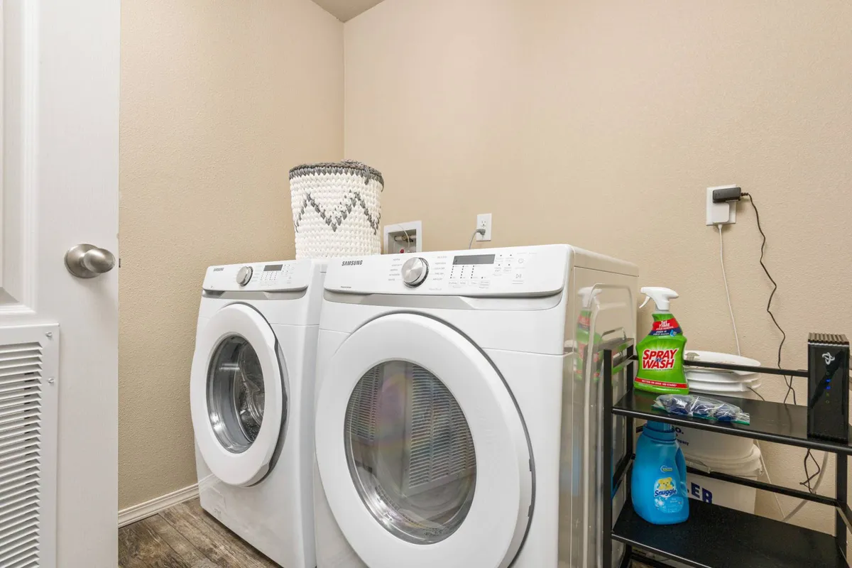 A practical laundry room with two white washing machines, a woven basket, and cleaning supplies on a shelf. The design is efficient and organized, supporting the ease of longer stays.