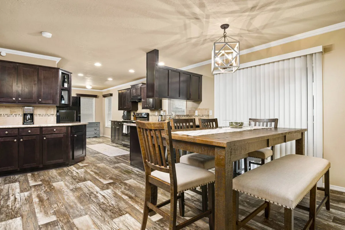 A cozy dining table set against warm kitchen cabinetry and illuminated by a stylish light fixture. The space exudes a welcoming ambiance suited for family meals, celebrations, or casual gatherings with friends, encouraging shared moments and conversation.