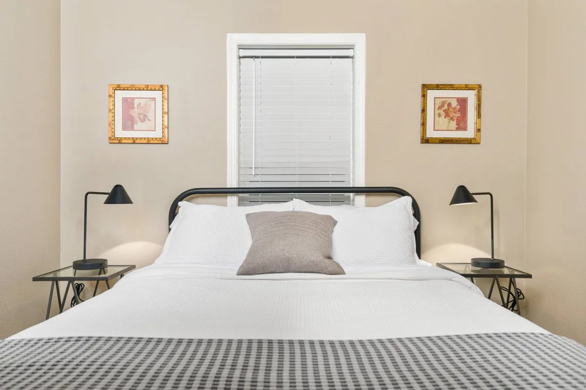A serene bedroom featuring a comfortable bed with crisp white bedding, framed artwork, and nightstands with soft-glowing lamps. The atmosphere is calm and restful—perfect for a good night's sleep to recharge for the next day's outdoor journey.