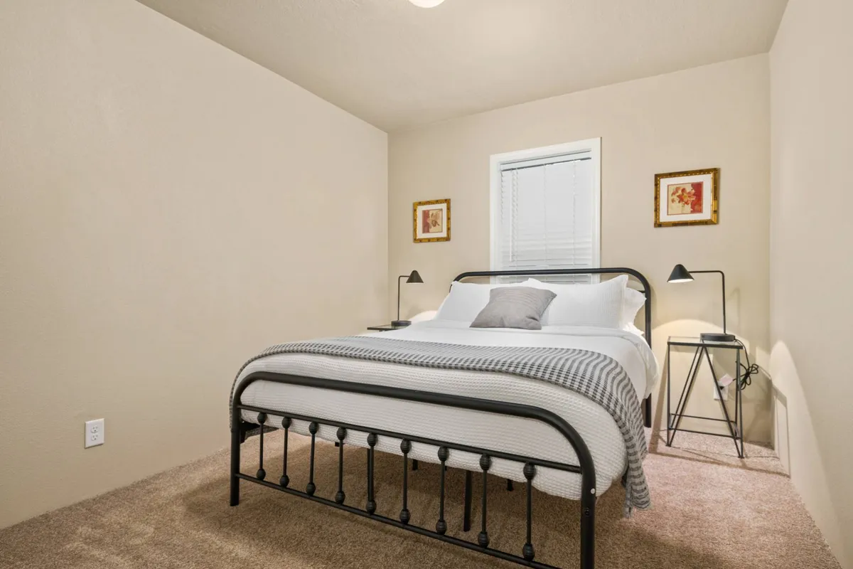 A cozy bedroom with a queen-sized bed dressed in inviting linens, accompanied by a nightstand, artwork, and a softly glowing lamp. The atmosphere is calm and welcoming, ideal for recharging after a day of adventure.